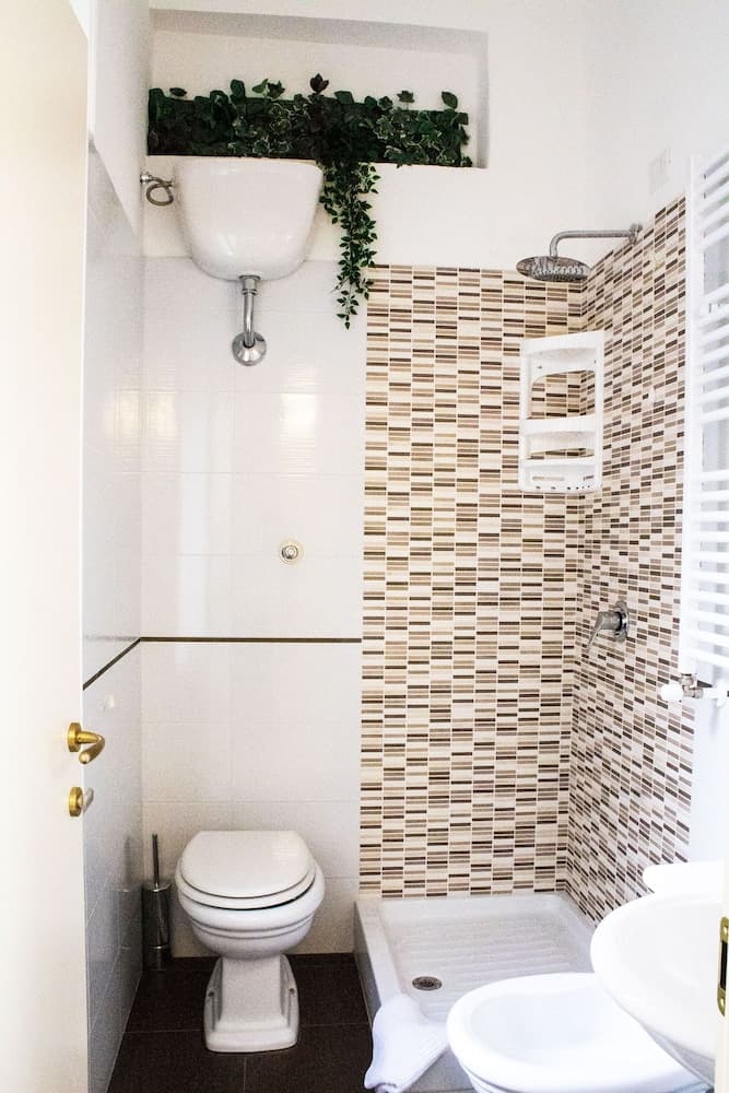 A cozy bathroom with mosaic-tiled walls, a sleek toilet, a sink adorned with greenery, and a modern shower setup, ideal for travelers seeking comfort and style in compact spaces.