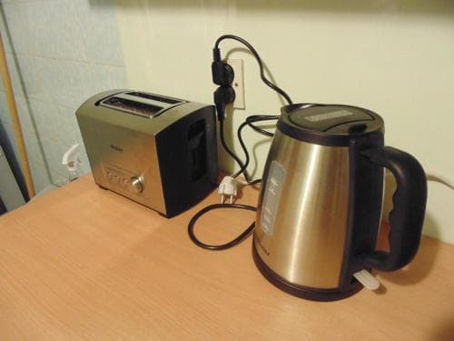 A cozy kitchen corner features a stainless steel kettle and toaster plugged into a wall outlet on a wooden countertop, ideal for travelers seeking a simple breakfast setup in a budget-friendly accommodation.
