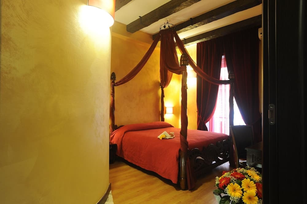 A cozy bedroom with warm yellow walls, wooden beams, a red canopy bed, and vibrant flowers creates an inviting atmosphere ideal for romantic getaways or luxurious stays.