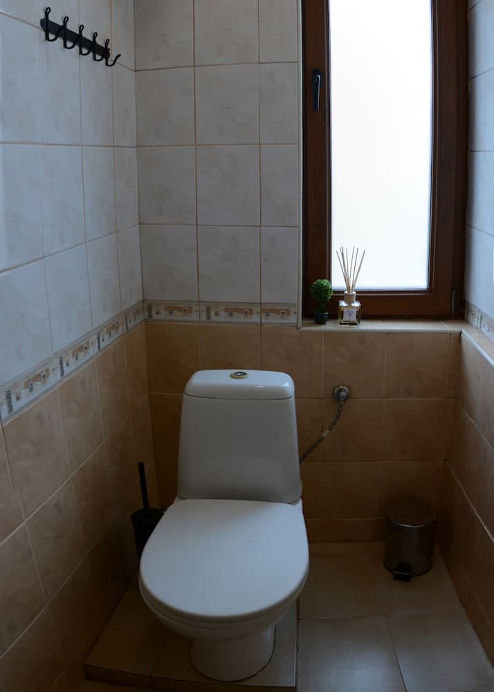 A cozy bathroom with beige tiled walls, a white toilet, a small window letting in soft light, and decorative elements like a reed diffuser and a mini plant, ideal for travelers seeking a clean and serene accommodation space.