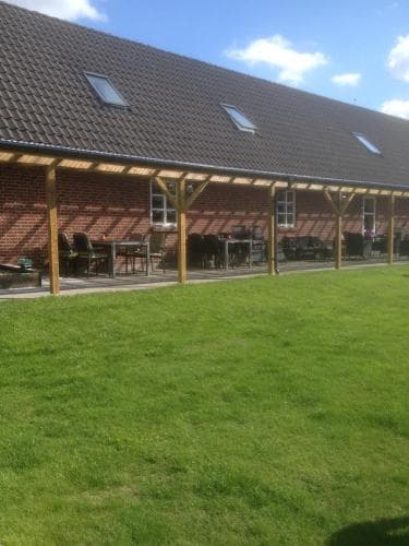 A serene rural retreat features a brick building with a wooden pergola and outdoor seating, set against a lush green lawn under a bright blue sky, ideal for a peaceful countryside getaway.