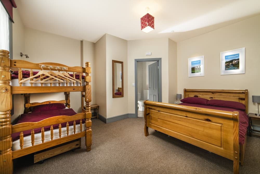 A cozy hotel room features wooden bunk beds and a single bed with burgundy bedding, a red pendant light, framed wall art, and a mirror, ideal for family travelers seeking comfort and functionality.
