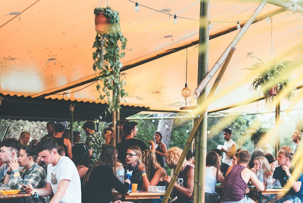 A lively outdoor dining area under a tent adorned with hanging plants and string lights creates a cozy, festive atmosphere perfect for social gatherings and events.