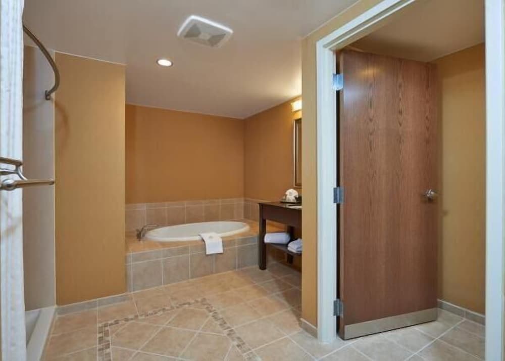 A cozy hotel bathroom features a tiled floor, a bathtub with a towel draped over the edge, warm beige walls, and a wooden door, ideal for travelers seeking relaxation and comfort.
