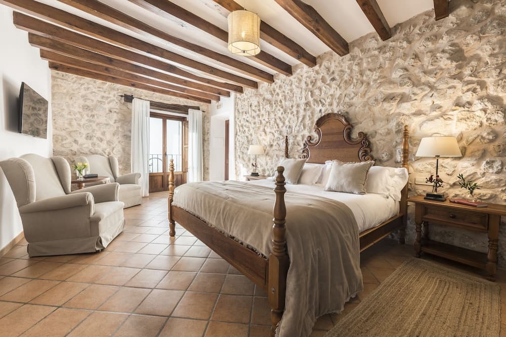 A cozy rustic bedroom with stone walls, wooden beams, and tiled floors exudes warmth and charm, perfect for travelers seeking a serene retreat in a boutique hotel.