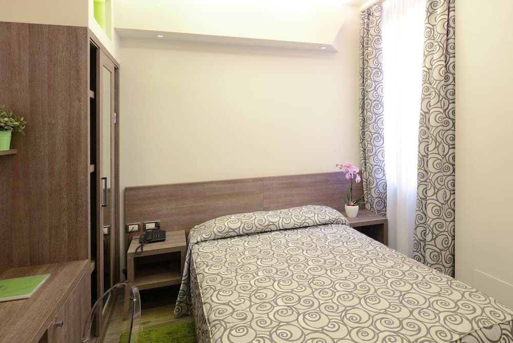 A cozy hotel room features a neatly made bed with patterned bedding, wooden furnishings, and soft lighting, creating a serene atmosphere ideal for travelers seeking comfort and relaxation.