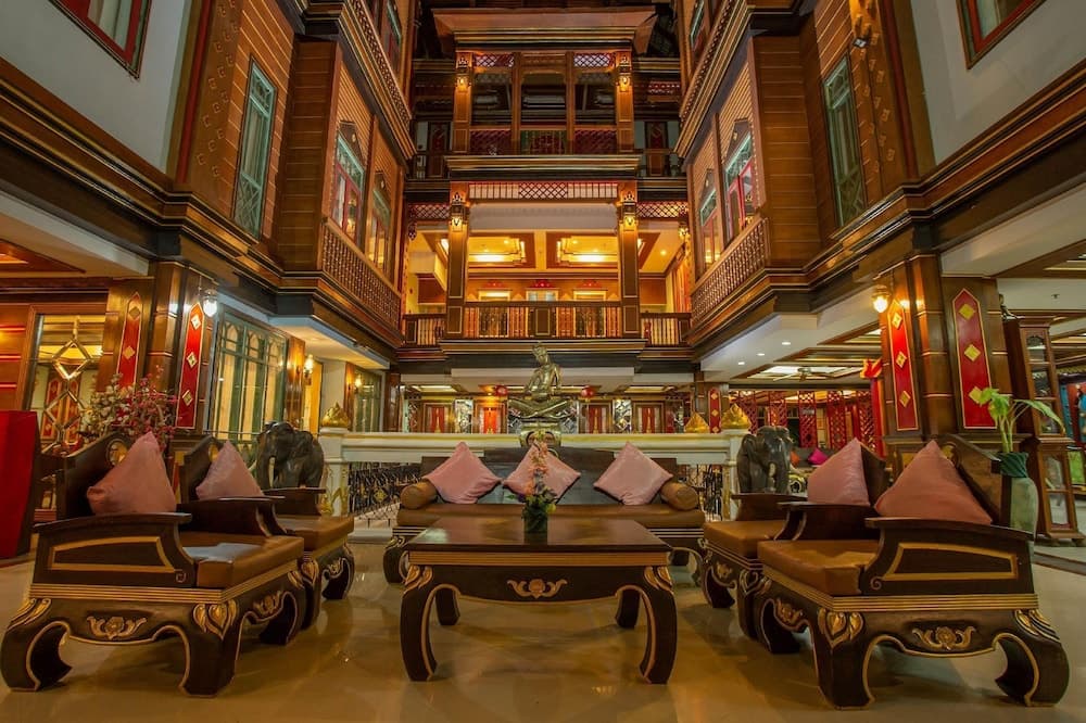 A luxurious indoor atrium with ornate wooden balconies, plush seating adorned with pink cushions, and a central Buddha statue creates an inviting atmosphere ideal for travelers seeking a serene and culturally rich accommodation experience.