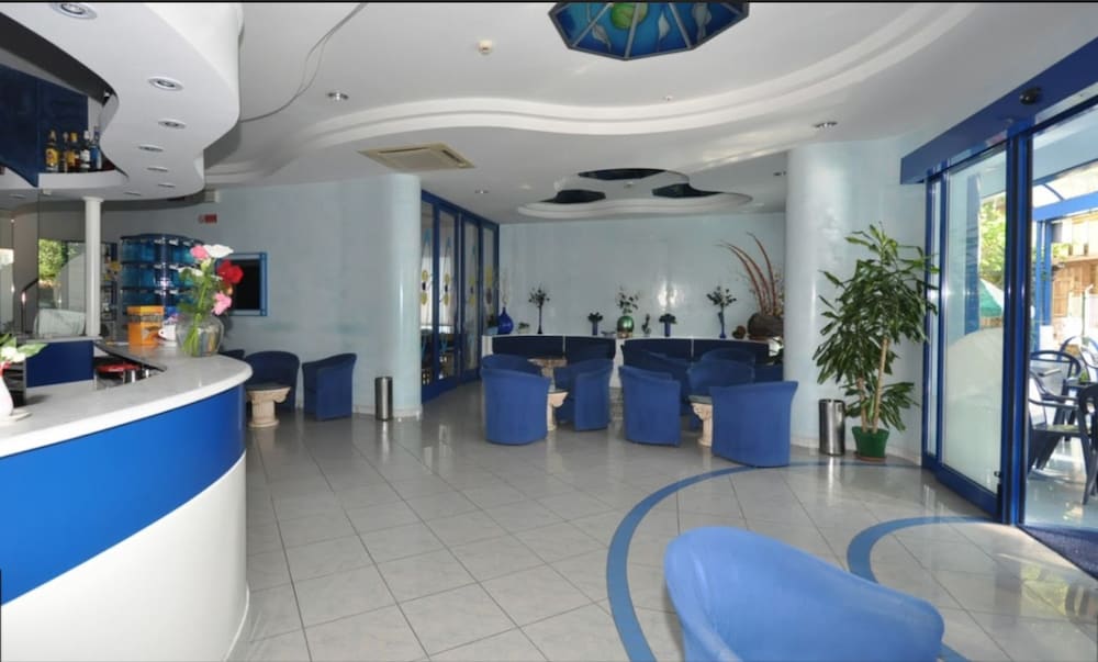 A serene hotel lobby features blue and white decor, comfortable seating, potted plants, and a reception desk, ideal for travelers seeking a relaxing atmosphere during their stay.