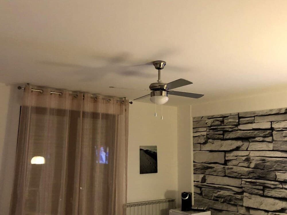 A cozy indoor living space features a ceiling fan, sheer curtains, a stone-textured wall, and ambient lighting, ideal for travelers seeking a comfortable and stylish accommodation.