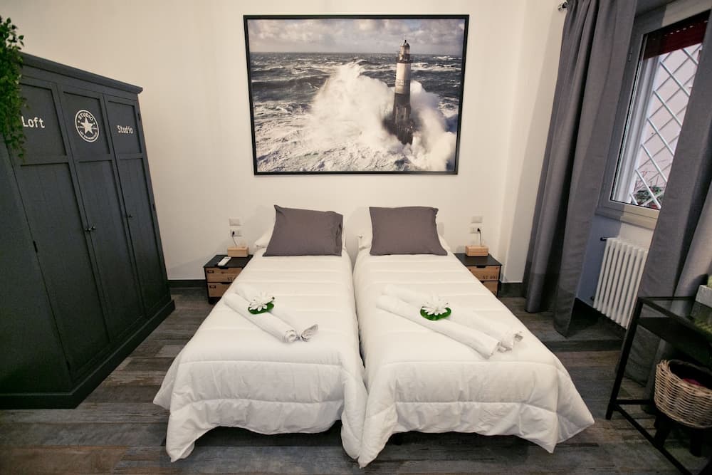 A cozy hotel room features twin beds adorned with neatly folded towels shaped like flowers, a large lighthouse artwork, and modern furnishings, ideal for travelers seeking comfort and style.