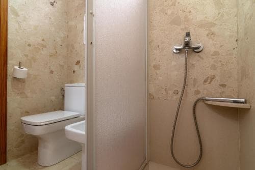 A cozy bathroom with beige marble walls features a toilet, sink, and handheld showerhead, ideal for travelers seeking comfort in compact spaces.