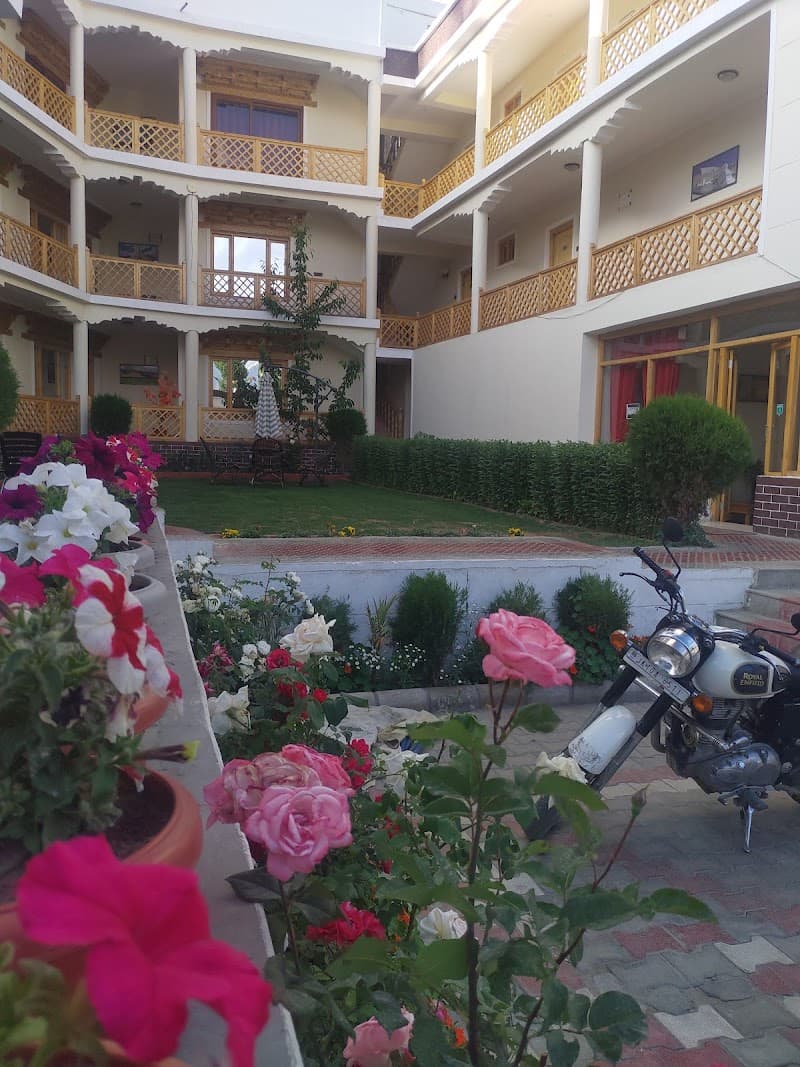 A serene courtyard at Hotel Ladakh Inn in Leh features vibrant flowers, lush greenery, and traditional balconies, creating an inviting atmosphere ideal for travelers seeking relaxation and cultural immersion.