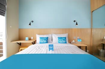 A cozy hotel room with a neatly made bed adorned with blue "airy" pillows, wooden bedside tables, and a serene blue wall, ideal for travelers seeking comfort and relaxation.