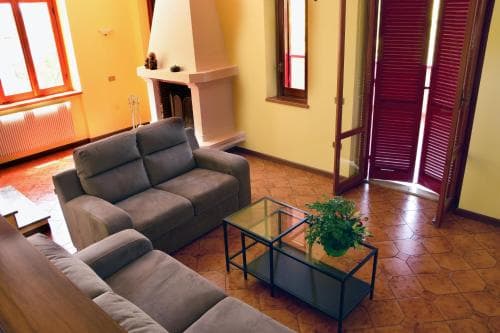 A cozy living room with warm yellow walls, a fireplace, comfortable sofas, and a glass coffee table creates an inviting atmosphere ideal for travelers seeking a relaxing retreat in a charming apartment setting.
