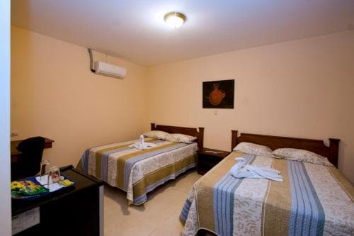 A cozy hotel room features two neatly made beds with striped linens, a small desk with colorful brochures, and warm lighting, ideal for travelers seeking comfort and convenience.