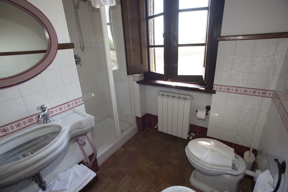 A cozy bathroom with white tiled walls, wooden accents, and natural light from a window offers a serene retreat for travelers seeking comfort and cleanliness.