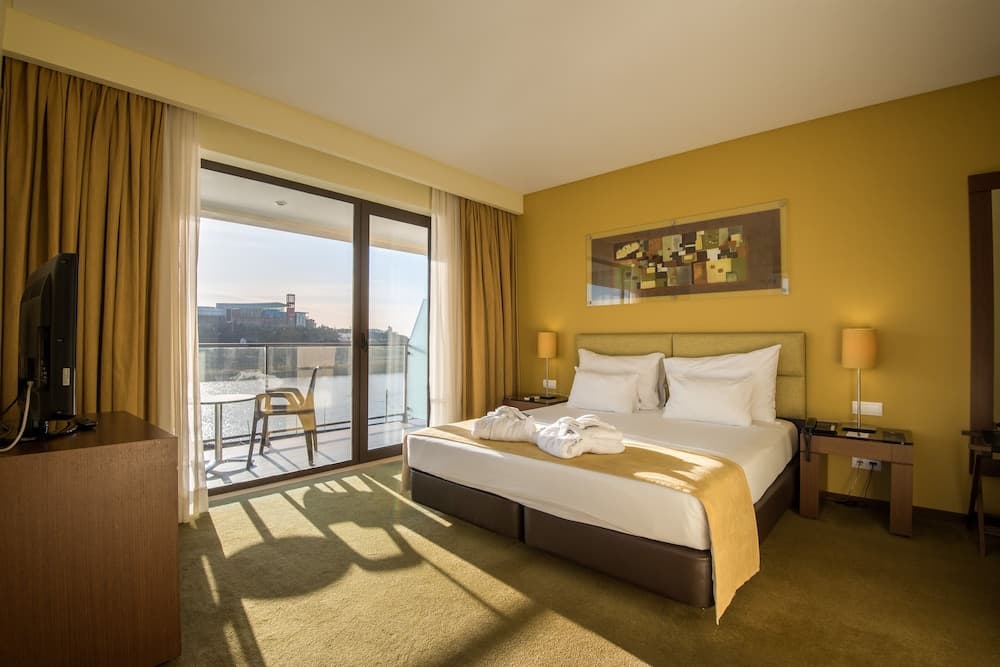 A cozy hotel room with warm yellow walls, a neatly made bed, and a balcony overlooking water, ideal for travelers seeking comfort and scenic views.