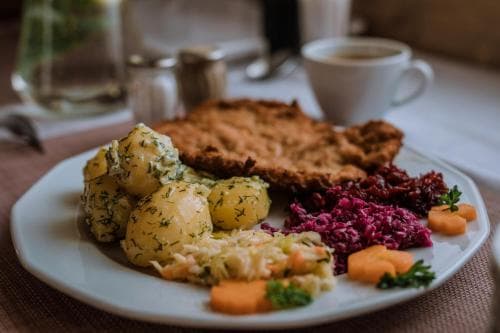 A cozy dining table scene features a hearty plate of schnitzel, potato salad, red cabbage, and carrots, perfect for a comforting culinary adventure in a traditional European restaurant setting.