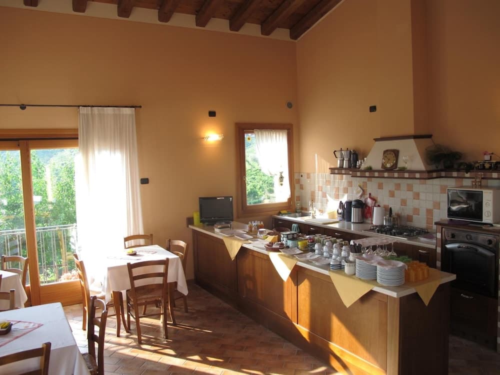 A cozy, sunlit kitchen-dining area with wooden beams, terracotta flooring, and a view of greenery through large windows, ideal for travelers seeking a warm, rustic retreat.