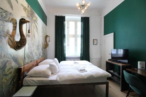 A cozy hotel room with vibrant green walls, a large bed adorned by an artistic wall mural of camels, and modern amenities like a TV and desk, perfect for travelers seeking comfort and charm in their accommodations.