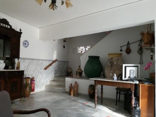 A cozy indoor space with rustic decor, featuring antique furniture, large ceramic jars, and a staircase, evokes a serene Mediterranean ambiance ideal for cultural exploration and relaxation.