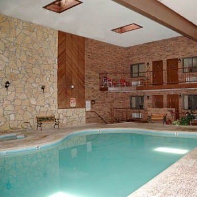 A cozy indoor pool area with stone walls, wooden accents, and balconies offers a serene retreat for travelers seeking relaxation in a hotel setting.