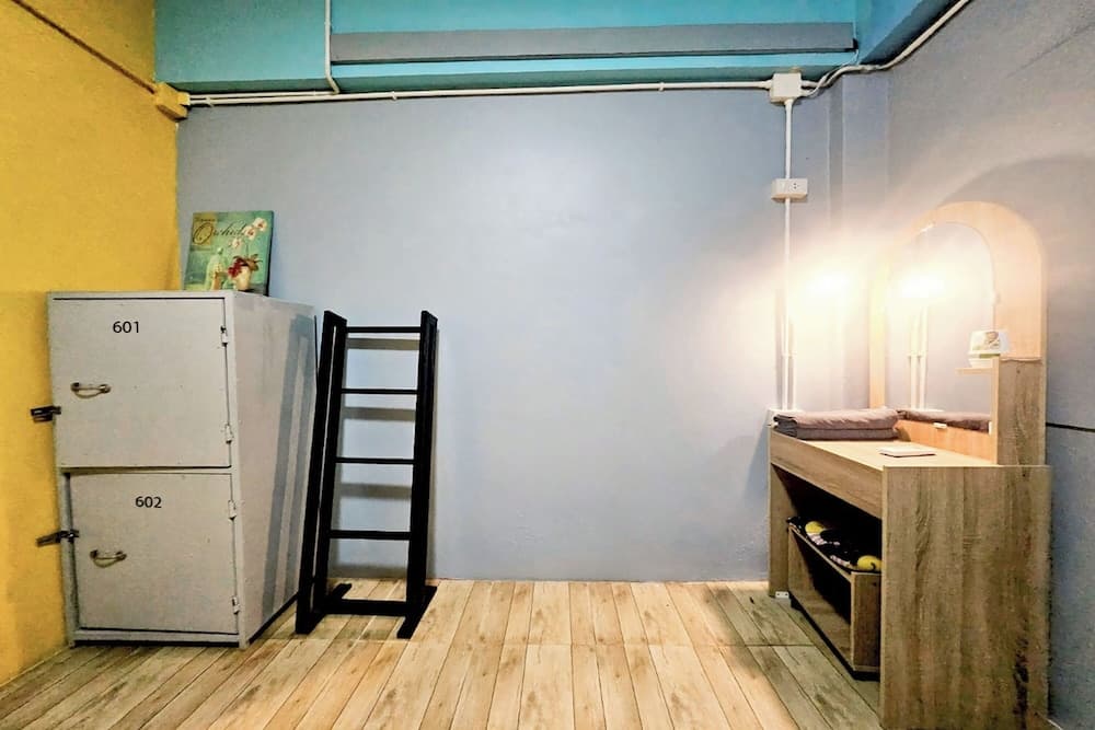 A cozy hostel room with wooden floors, lockers numbered 601 and 602, a ladder, and a warmly lit vanity area creates an inviting atmosphere for budget travelers seeking comfort and functionality.