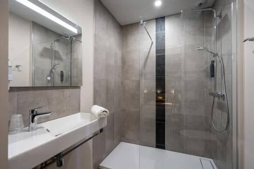 A modern bathroom with sleek tiled walls, a glass-enclosed shower, and a minimalist sink setup creates a clean and serene atmosphere, ideal for travelers seeking comfort in a hotel or vacation rental.
