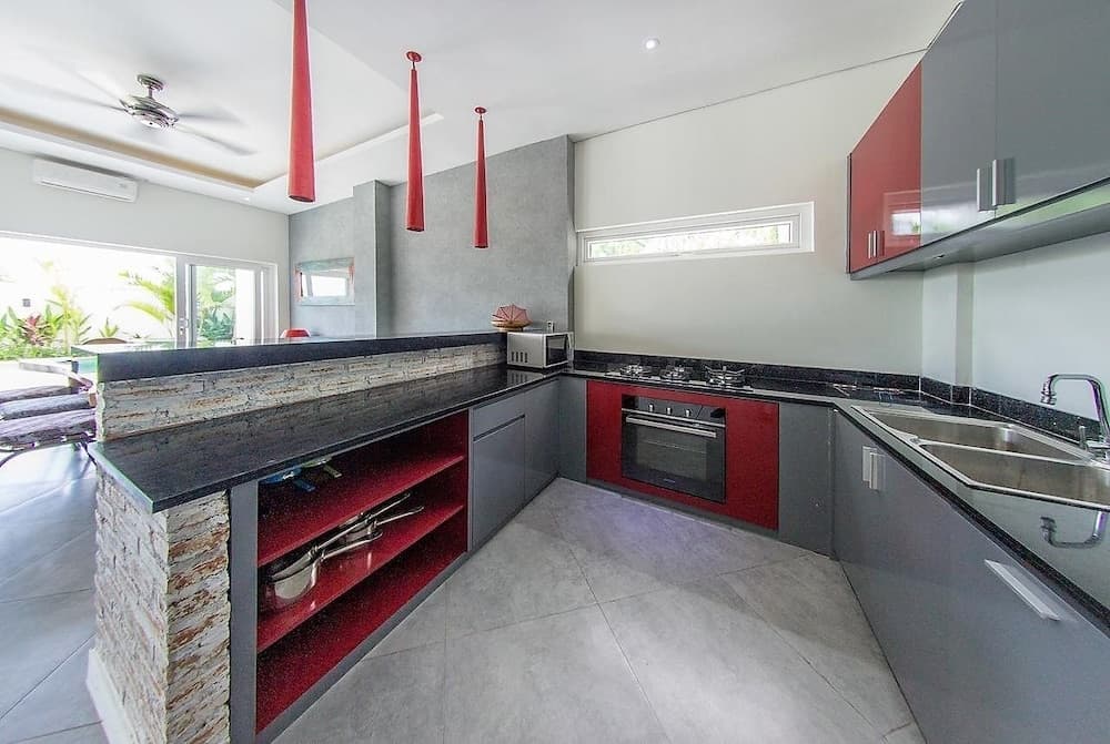 A modern kitchen with sleek gray and red cabinetry, stone countertops, and vibrant red pendant lights creates an inviting atmosphere ideal for luxury vacation rentals.