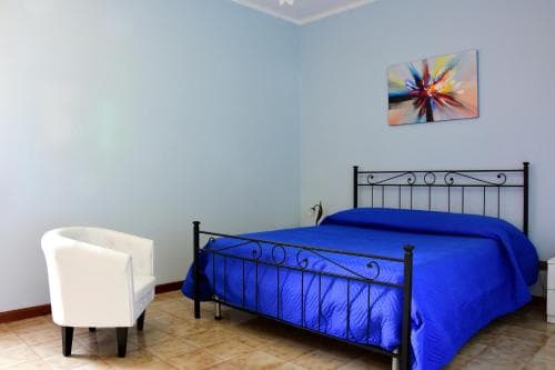 A cozy bedroom with light blue walls, a vibrant blue bedspread, a white armchair, and abstract wall art creates a serene atmosphere, ideal for travelers seeking a tranquil accommodation experience.