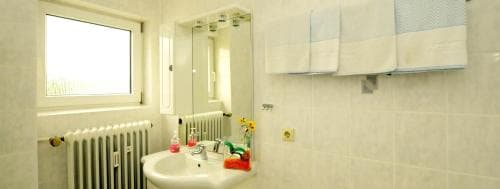 A cozy hotel bathroom features a bright window, tiled walls, neatly hung towels, and a sink adorned with colorful toiletries, ideal for travelers seeking comfort and cleanliness.