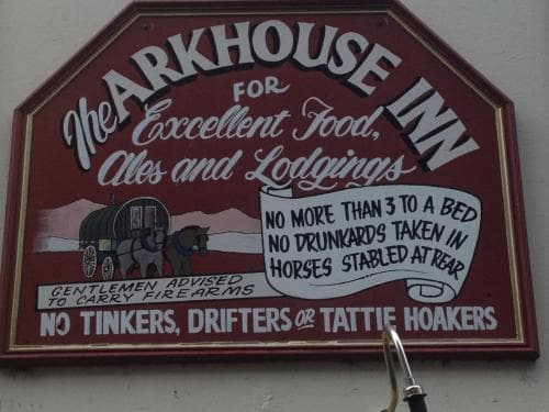 The Arkhouse Inn sign, featuring a rustic wagon illustration and humorous vintage rules, sets a quirky, historical mood ideal for travelers seeking unique lodging experiences in a themed setting.