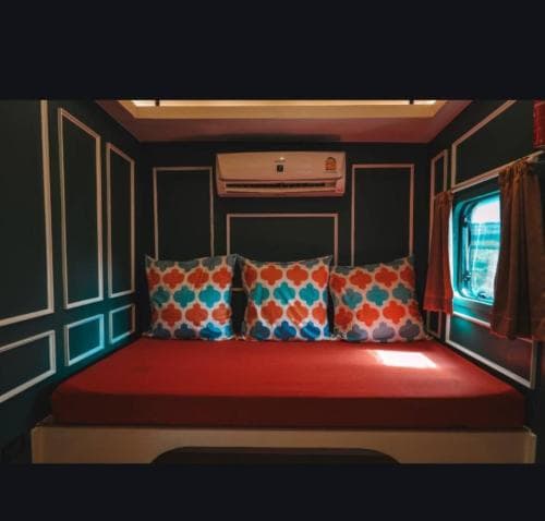 A cozy camper interior features a vibrant red bed adorned with patterned pillows, set against dark paneled walls under warm lighting, ideal for travelers seeking comfort in compact spaces.