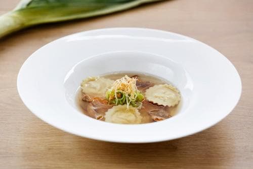 A beautifully presented bowl of delicate soup garnished with herbs and crispy elements sits invitingly on a wooden table, perfect for culinary enthusiasts exploring gourmet dining experiences.
