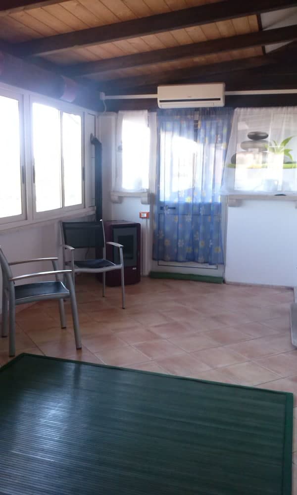 A cozy indoor space with wooden beams, tiled flooring, and large windows draped with floral curtains offers a serene retreat, ideal for travelers seeking relaxation in a vacation rental.