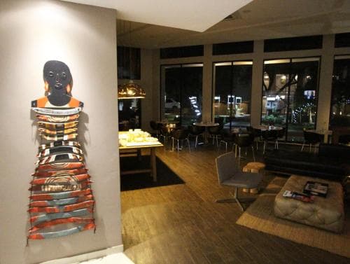 A cozy café lounge features modern art on the walls, plush seating by large windows, and a warm ambiance ideal for travelers seeking a relaxing spot to unwind or work remotely.