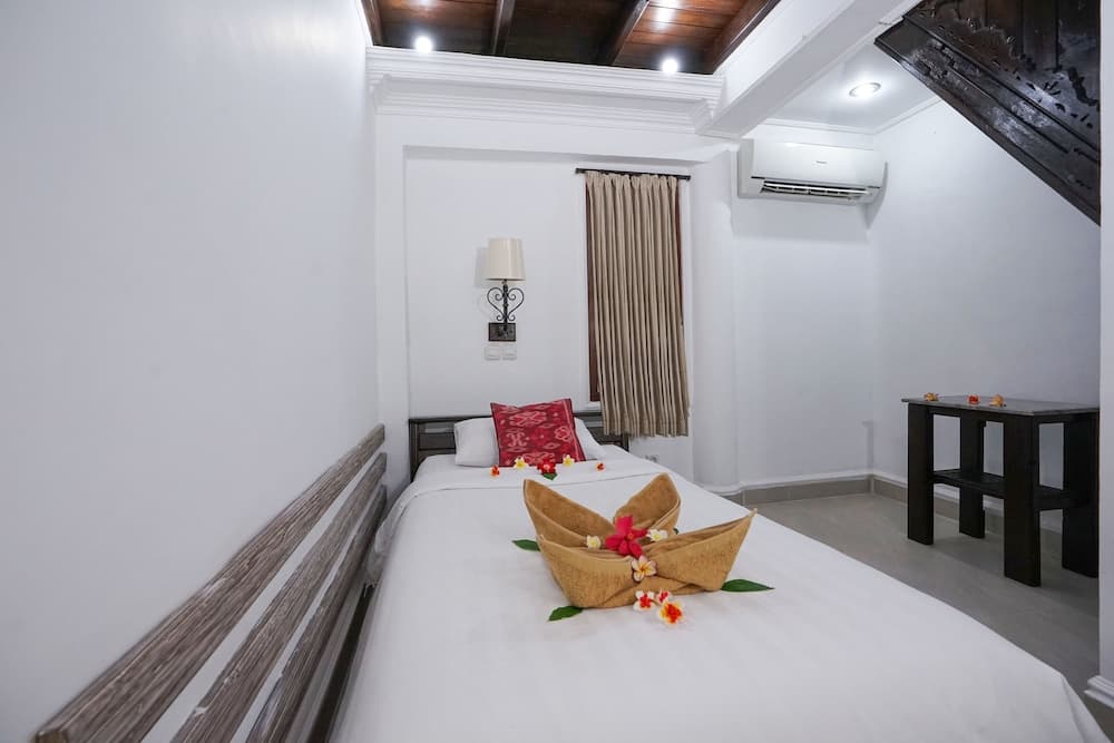 A cozy hotel room with white walls, wooden accents, a neatly made bed adorned with floral decorations, and modern amenities creates a serene atmosphere ideal for travelers seeking relaxation.