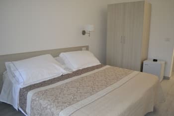 A cozy hotel room features a neatly made bed with white linens and a decorative throw, complemented by a modern wardrobe and bedside table, ideal for travelers seeking comfort and simplicity.