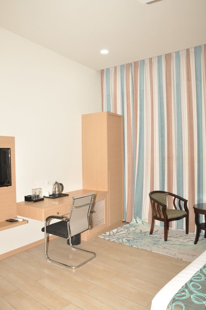 A cozy hotel room features a wooden desk with a kettle set, striped curtains, and comfortable seating, creating a serene atmosphere ideal for travelers seeking relaxation and productivity.