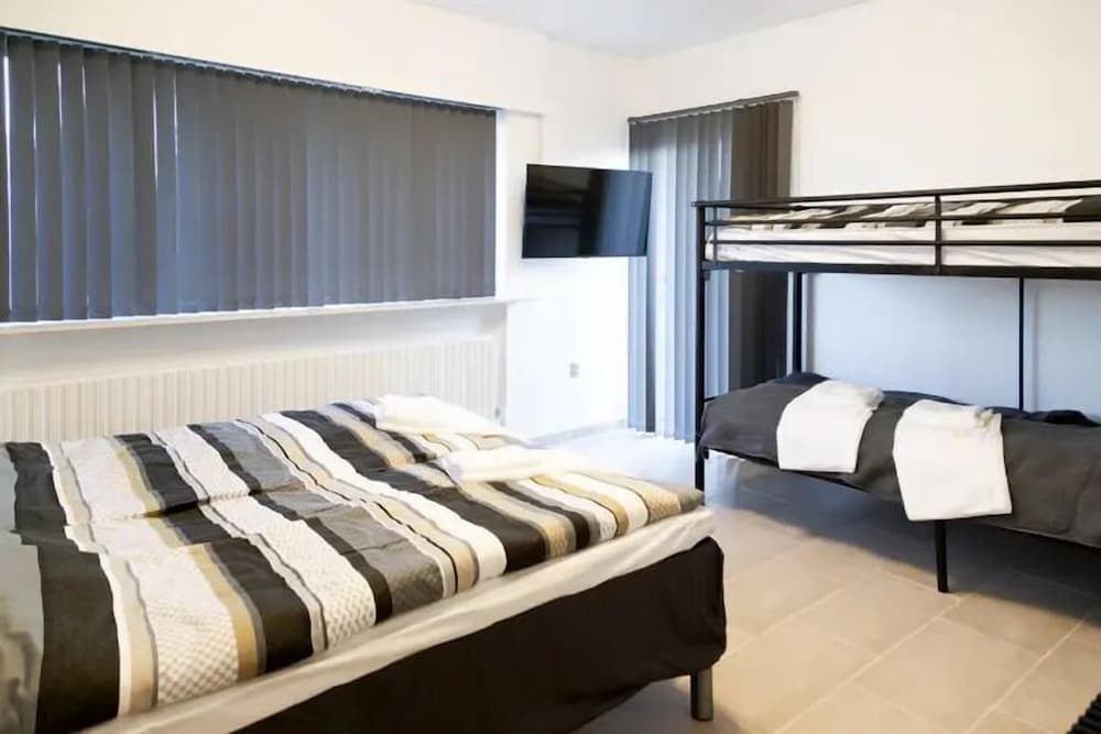 A cozy hostel room features a neatly made bed with striped bedding, a bunk bed, and a mounted TV, ideal for budget travelers seeking comfort in a minimalist setting.