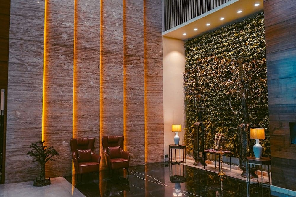 A luxurious hotel lobby features sleek marble walls illuminated by warm lighting, cozy leather chairs, and a vibrant living wall adorned with decorative sculptures, creating an inviting atmosphere ideal for travelers seeking comfort and elegance.