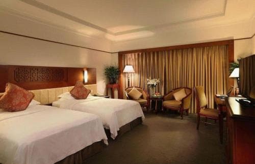 A cozy hotel room features two neatly made beds, warm lighting, and elegant furnishings, creating an inviting atmosphere ideal for travelers seeking comfort and relaxation.
