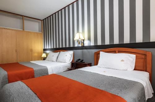 A cozy hotel room features two neatly made beds with orange accents against a striking black-and-white striped wall, ideal for travelers seeking comfort and style.