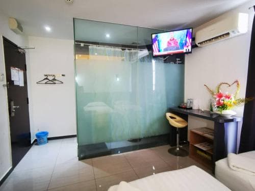 A cozy hotel room features a modern glass-enclosed bathroom, a small dining area with vibrant flowers, and a mounted TV, ideal for travelers seeking comfort and convenience in an urban setting.