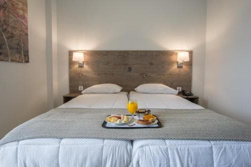 A cozy hotel room features a neatly made bed with a wooden headboard, soft lighting, and a breakfast tray of pastries and juice, inviting travelers to enjoy a relaxing morning getaway.