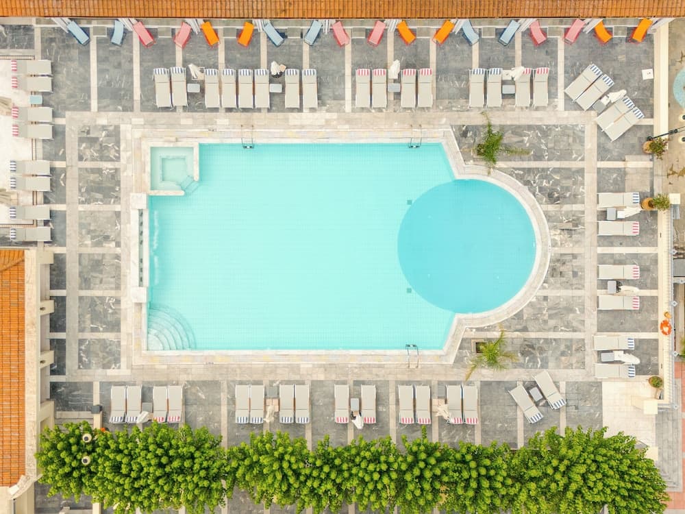 An aerial view of a serene hotel pool area surrounded by neatly arranged lounge chairs and vibrant greenery, ideal for travelers seeking relaxation and leisure.