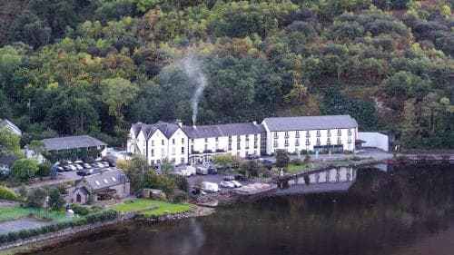 A serene lakeside hotel nestled among lush green hills, featuring steam rising from its chimney, ideal for tranquil retreats and nature-inspired getaways.