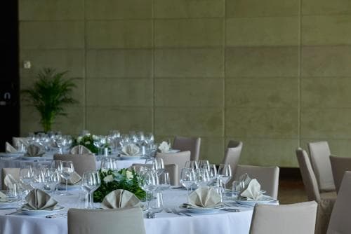 A serene banquet hall with neatly arranged tables, elegant glassware, and fresh greenery creates an inviting atmosphere ideal for corporate events or formal gatherings.