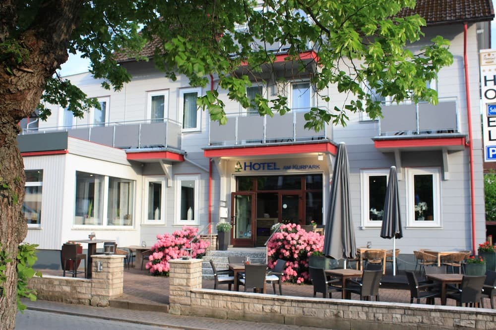 A charming hotel with outdoor seating, blooming pink flowers, and lush greenery offers a cozy and inviting atmosphere for travelers seeking relaxation in a picturesque setting.