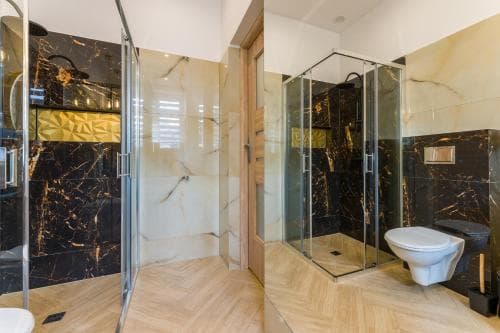 A luxurious bathroom with sleek black marble walls, a glass-enclosed shower, and warm wooden flooring exudes modern elegance, ideal for travelers seeking upscale accommodations.